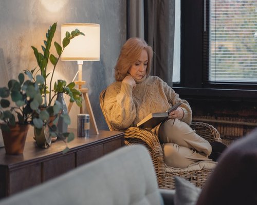 A person sitting in a cozy armchair reading a book next to a lamp